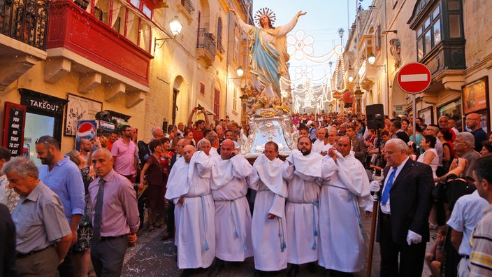 Menschen ziehen in einer Prozession mit einer Heiligenfigur durch eine Straße