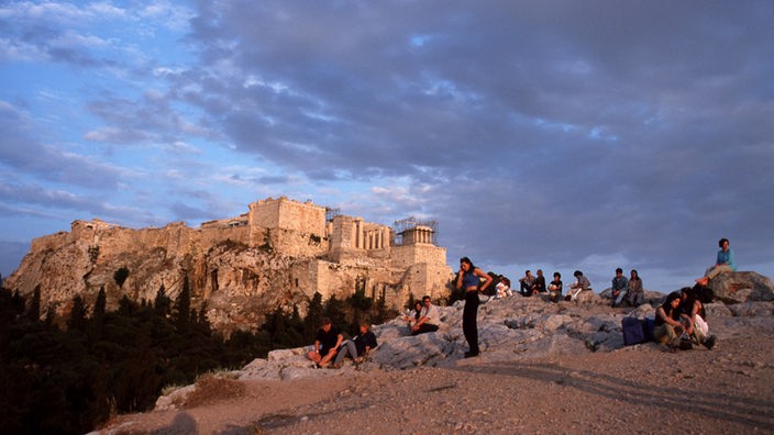 Steiniges Felsplateau mit Touristen, im Hintergrund die Akropolis