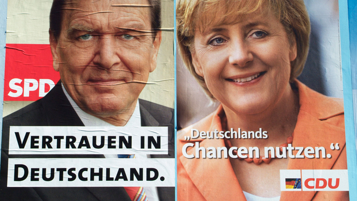 Zwei nebeneinander hängende Wahlplakate mit Schröder und Merkel; unter Schröders Bild steht 'Vertrauen in Deutschland', unter Merkels Bild 'Deutschlands Chancen nutzen'.