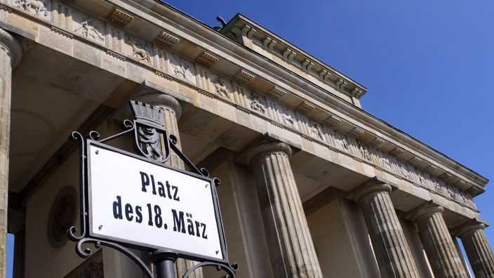 Ein Straßenschild mit der Aufschrift "Platz des 18. März" vor blauem Himmel am Brandenburger Tor