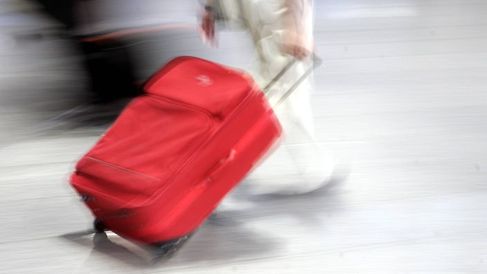 Person zieht einen roten Rollkoffer
