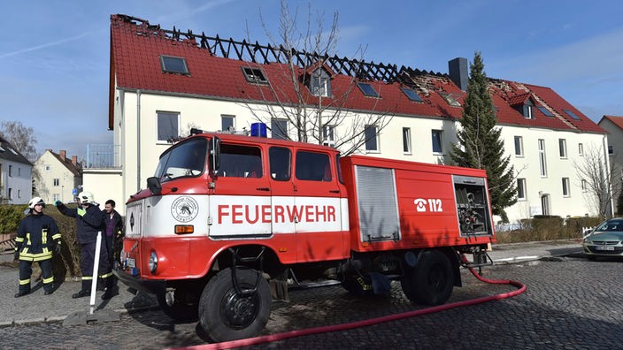 Feuerwehrwagen vor einem Haus mit ausgebranntem Dachstuhl.