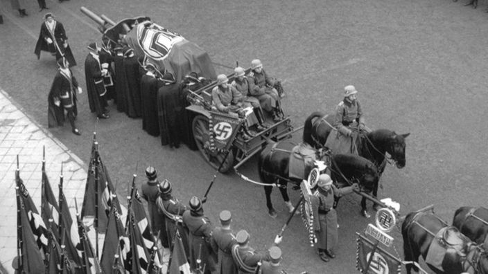 Schwarzweiß-Bild: Auf dem Wagen einer Kutsche ist der Sarg von Ernst vom Rath aufgebahrt, zugedeckt mit einer Hakenkreuz-Fahne.