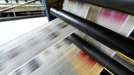 Zeitungsseiten rollen in Bewegungsunschärfe durch eine moderne Druckerpresse.