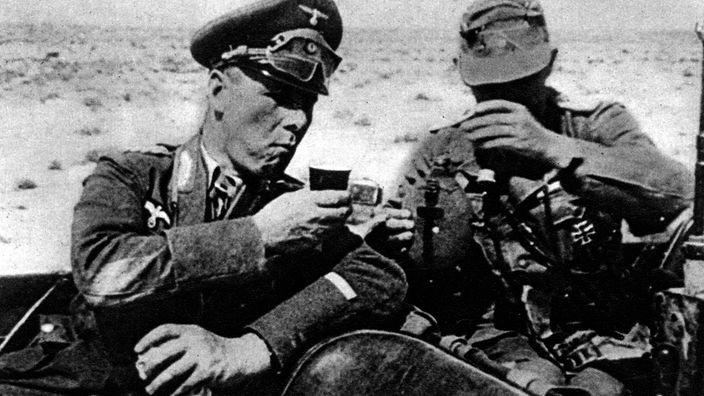 schwarz-weiß-Aufnahme von Rommel in Uniform mit Soldat rechts neben sich.