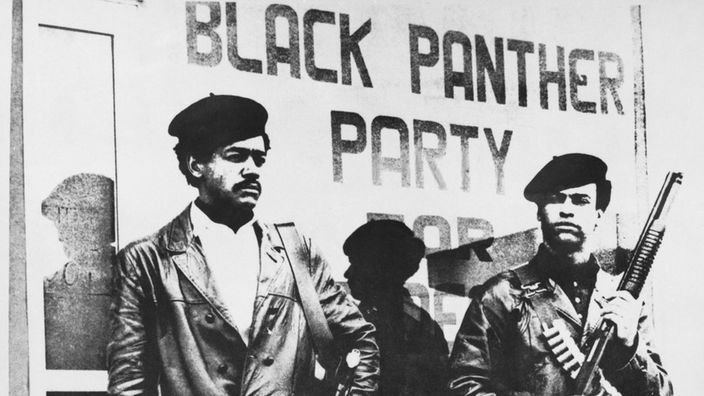 Schwarzweiß-Foto: Zwei bewaffnete Schwarze vor dem Schriftzug "Black Panther Party"
