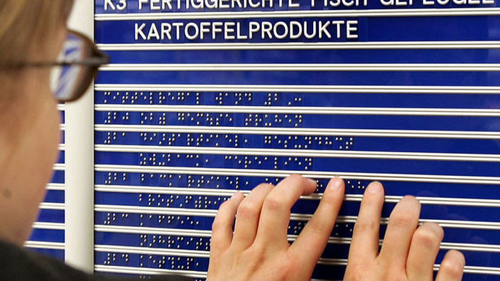 Eine Frau ertastet die Braille-Schrift auf einer blauen Tafel. Auf der Tafel steht, wo sich die verschiedenen Waren in einem Supermarkt befinden. | Bildquelle: ddp Eine Frau ertastet die Braille-Schrift auf einer blauen Tafel. Auf der Tafel steht, wo sich die verschiedenen Waren in einem Supermarkt befinden.