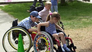 Kinder mit körperlicher Behinderung spielen miteinander im Rollstuhl.