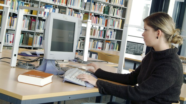 Junge Frau sitzt in einer Bibliothek vor einem Computerbildschirm