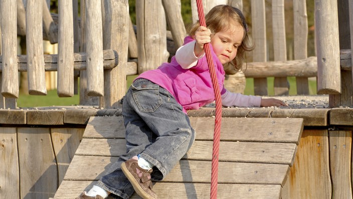 Mädchen klettert an Seil auf ein Holzhaus