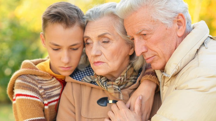 Enkel und Großvater umarmen Großmutter mit betrübten Gesichtern