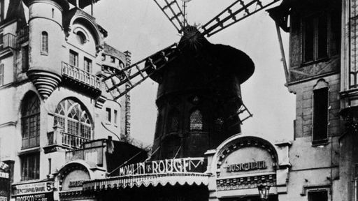 Auf der Schwarzweiß-Fotografie sieht man das französische Varieté Moulin Rouge. Von außen sieht es aus wie eine Windmühle.