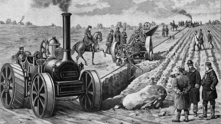 Zeichnung eines Dampfpfluges aus dem 19. Jahrhundert am Rand eines Feldes. Um ihn herum stehen einige Männer in Anzügen.