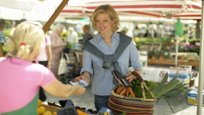 Frau bezahlt in einem Wochenmarkt die Händlerin am Gemüse- und Obststand.