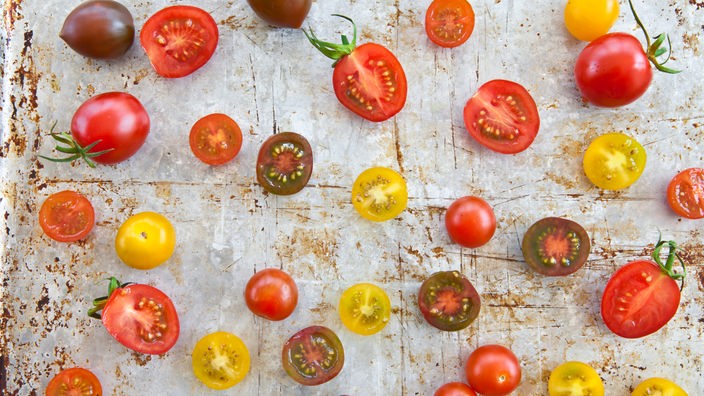 Tomaten und Tomatenstücke liegen auf einem Küchenbrett.