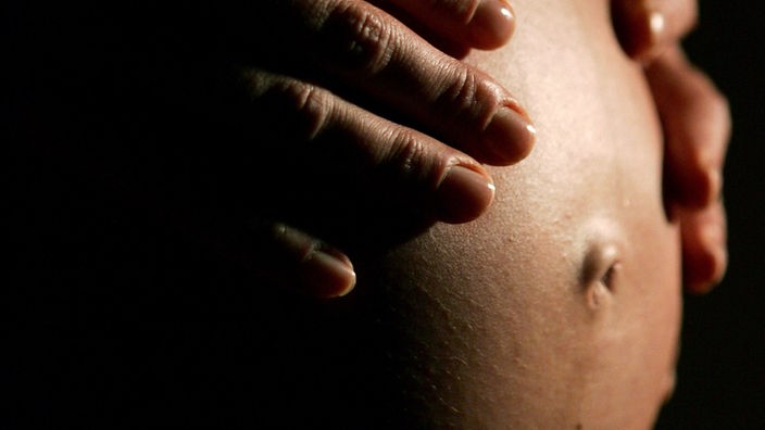Eine hochschwangere Frau fasst sich mit beiden Händen an ihren Bauch