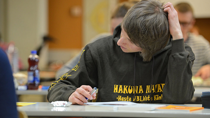 Ein Schüler sitzt an einem Tisch vor seiner Abituraufgabe.