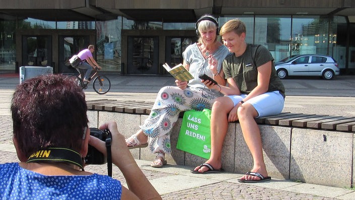 Auf einer Bank sitzen ein Jugendlicher und eine ältere Dame vor dem Leipziger Gewandhaus nebeneinander