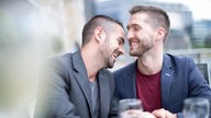 Ein junges Paar in einem Café: die beiden Männer lachen zusammen.