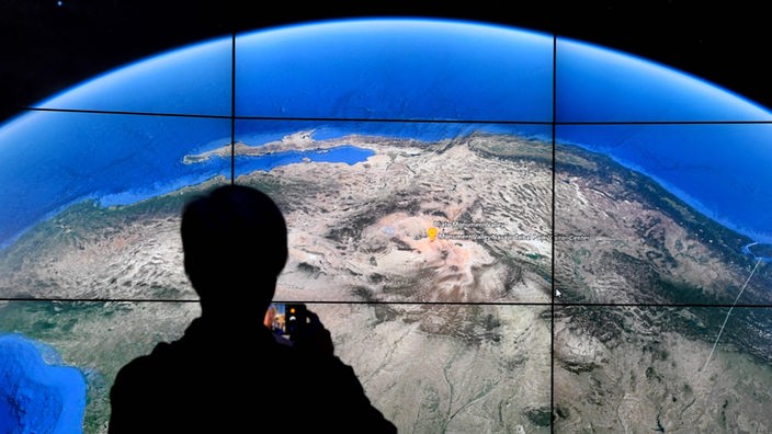 Ein Besucher steht in einem Museum vor einem großen Bildschirm mit Satellitenbild