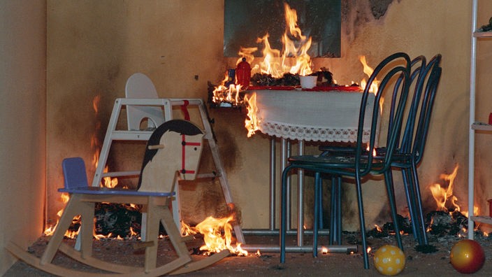 Ein Tischchen mit brennendem Adventskranz. Davor zwei Stühle, ein Kinderhochstuhl und ein Schaukelpferd.