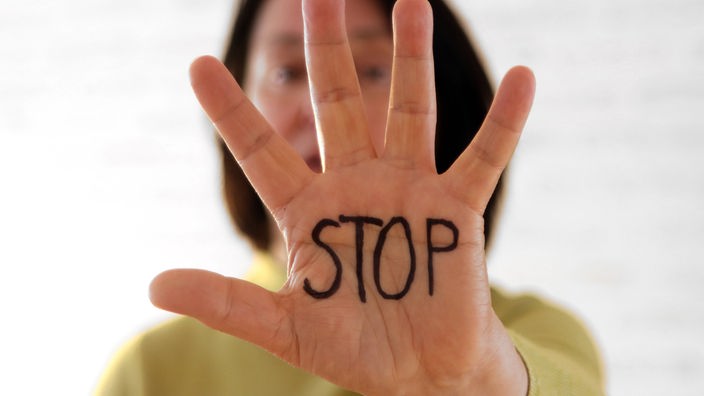 Frau hält Hand mit ausgetreckten Fingern vor sich hoch. Auf der Hand steht in Großbuchstaben: Stop.