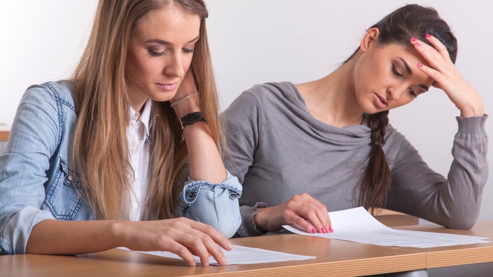 Zwei junge Frauen sitzen an einem Tisch und schreiben eine Prüfung.