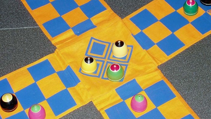 Kreuzförmiges Pachisi-Spielbrett aus Stoff. Auf dem Stoff sind quadratische Spielfelder in zwei Farben aufgedruckt.