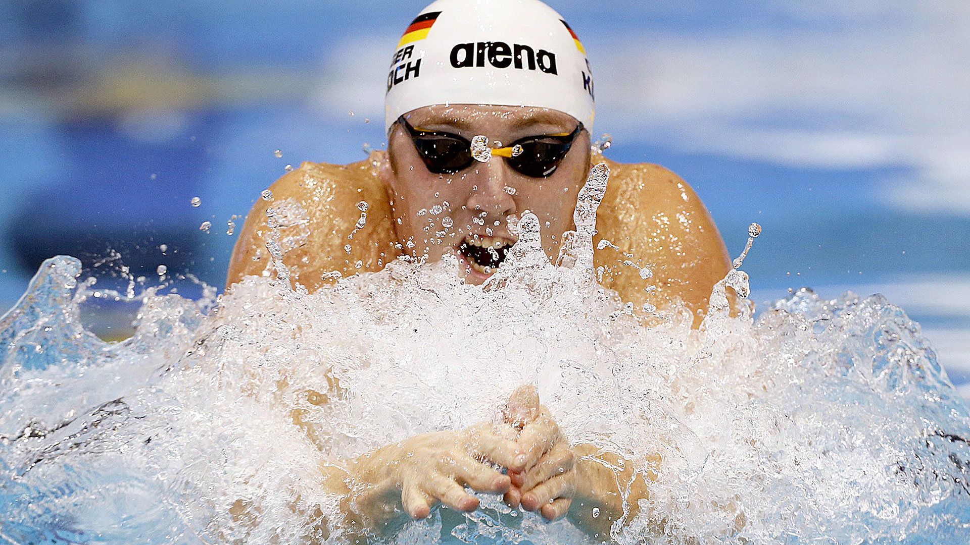 Eine Schwimmerin holt gerade beim Brustschwimmen Luft und ist mit Kopf und Armen über dem Wasser.