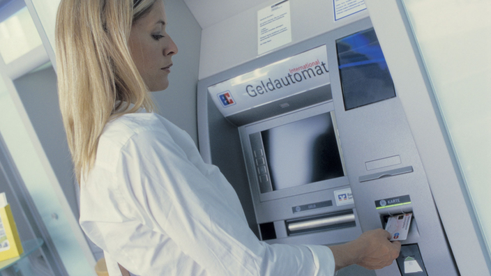 Eine junge Frau steht dicht an einem Geldautomat und hebt Geld ab