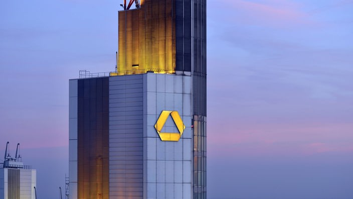 Das Dach des Commerbank Towers aus der Nähe im Abendlicht. Auf der Fassade prangt das gelbe Commerzbank-Logo.