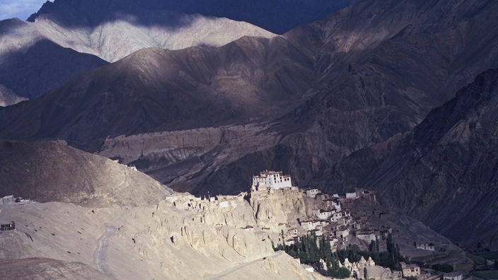 Blick auf die karge tibete Gebirgslandschaft. Auf einem Felssporn in der Mitte des Bildes liegt ein Kloster.