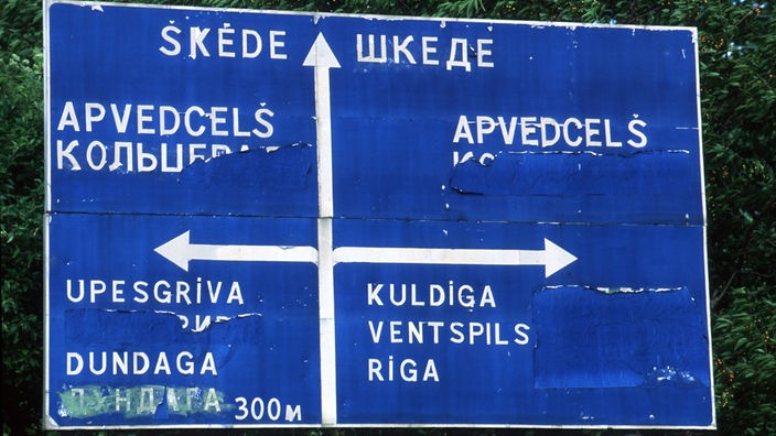 Straßenschild mit lettischer und teils überklebter russischer Schrift.