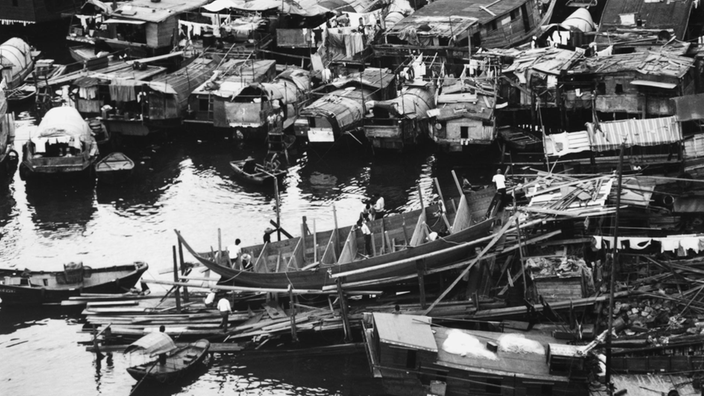 Schwarzweiß-Foto von zahlreichen kleinen Hausbooten, die durcheinander im Hafen stehen.