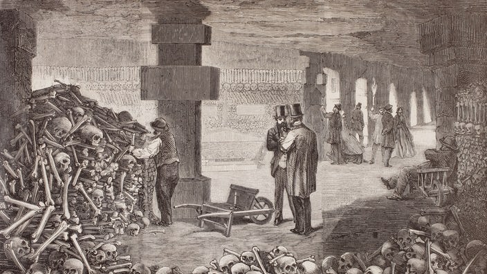 Historischer Stich: Menschen in den Pariser Katakomben, umgeben von Totenschädeln und Gebeinen.