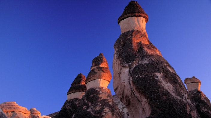 Drei Felskegel, die an ihrer Spitze so aussehen, als ob sie einen Hut aus Basalt tragen würden