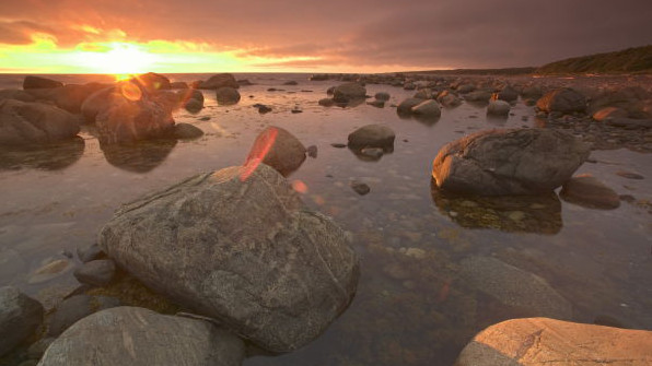 Felsbrocken liegen am Ufer im Gros Morne Nationalpark im rötlichen Licht der untergehenden Sonne.