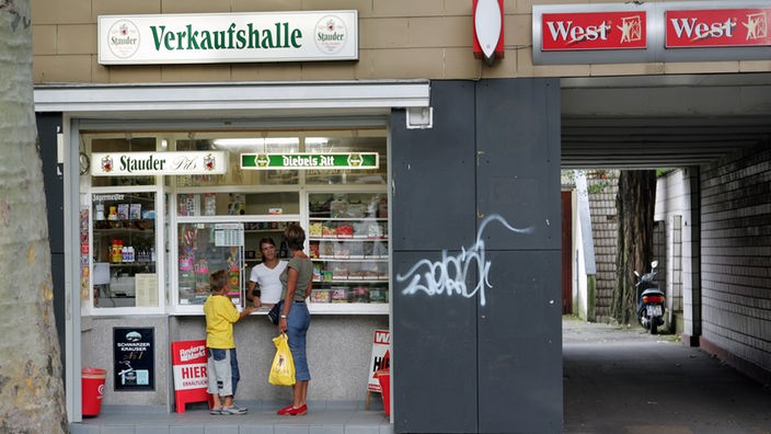 Kiosk im Ruhrgebiet mit dem Schild 'Verkaufshalle'. Eine Mutter mit ihrem Kind unterhält sich mit dem Besitzer.