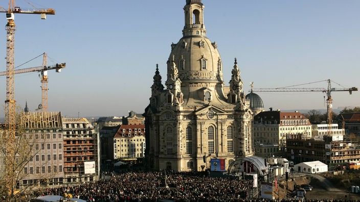 Das Bild zeigt die Frauenkirche am Tag ihrer Wiedereinweihung. Tausende Schaulustige stehen vor dem Platz. Im Hintergrund sind noch Kräne zu sehen.