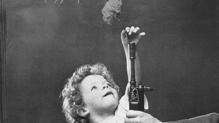 Ein kleines Mädchen steckt eine Nelke in einen Gewehrlauf.