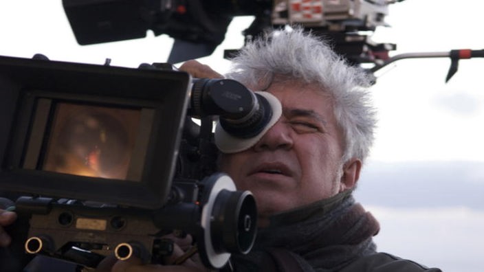 Almodóvar mit ergrautem Haar am Filmset von "Zerrissene Umarmungen" (2009), er blickt durch eine Kamera.
