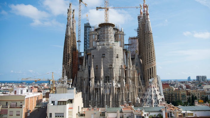 Frontaler Blick auf die Kirche "Sagrada Familia" mit einem Baukran an der Seite