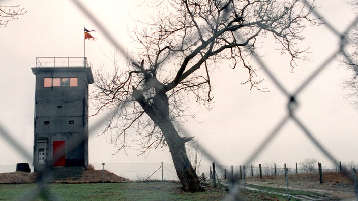 Auf einem flachen Hügel in Rüterberg steht ein Wachturm. Im Vordergrund ist ein Zaun zu sehen. | Bildquelle: dpa/Jens Büttner Auf einem flachen Hügel in Rüterberg steht ein Wachturm. Im Vordergrund ist ein Zaun zu sehen.