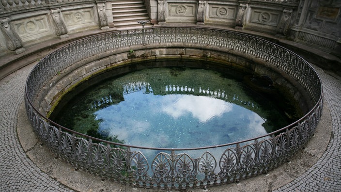 Ein Mann steht an der Einfassung der Donauquelle in Donaueschingen, die wie ein großer Brunnen gestaltet ist.