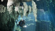 Eine Taucherin im Sistema Sac Actun in Mexiko schwimmt an weißen Tropfsteinen vorbei