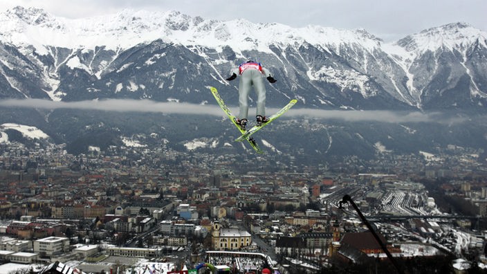 Ein Skispringer fliegt bei der Vierschanzentournee von der Bergiselschanze scheinbar über dem österreichischen Innsbruck mit seinen schneebedeckten Bergen im Hintergund.