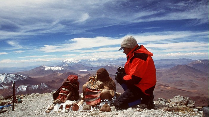 Ein Mann kniet neben zwei Inkamumien auf einem Gipfel der Anden.