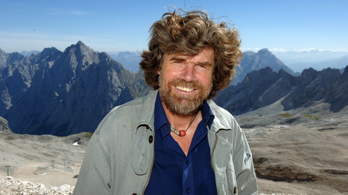 Lachender Reinhold Messner vor Gebirgspanorama.