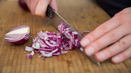 Großaufnahme von zwei Händen, die ein Messer halten und damit Zwiebeln schneiden