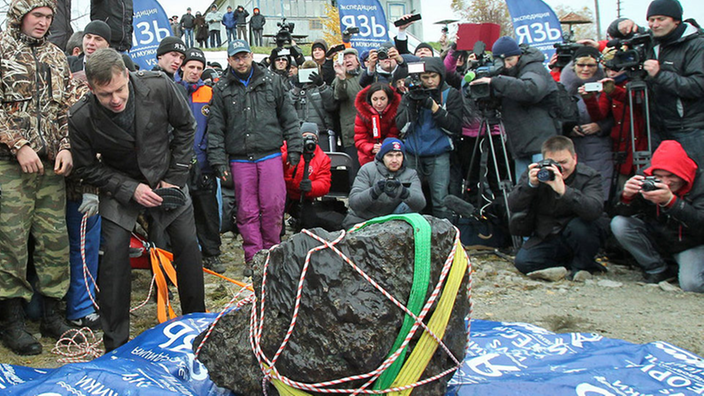 Eine Menschenmenge steht hinter einem Meteoriten, der 60 Kilometer westlich von Tscheljabinsk gefunden wurde.